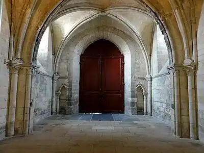 Même porte rouge vue de l'intérieur, dans une pièce vide surmontée d'une croisée d'ogives.