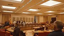 Une salle de réunion avec des fauteuils, des bureaux et des personnes.