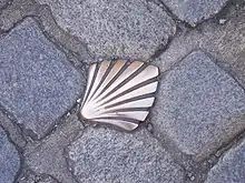 photographie d'une coquille Saint-Jacques en cuivre insérée dans les pavés d'une rue de Limoges et marquant le passage de la Via Lemovicensis menant à Saint-Jacques de Compostelle