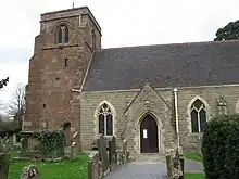 Photo d'un bâtiment aux murs de briques grises flanqué d'une grande tour carrée à gauche dont les briques sont rouges