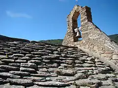 Photographie du toit de lauzes dominé par le petit clocher-mur doté d'une cloche.