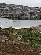 Photographies en couleurs de deux maisons implantées sur les rives d'un fjord, une étendue recouverte d'herbacées au premier plan.