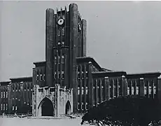 Photo noir et blanc d'un bâtiment en pierre étendu sur toute la largeur du cliché, avec une tour centrale exhibant une horloge sur chaque façade visible, sur fond de ciel clair.