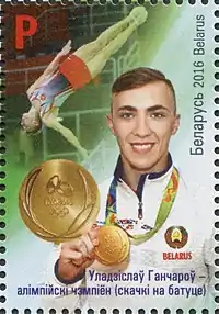 Un timbre représentant un homme avec une veste blanche tenant une médaille d'or avec en arrière-plan celui-ci en train de faire un salto tête en bas.
