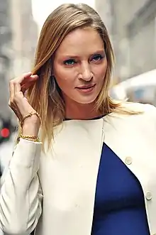 Photo d'Uma Thurman debout avec une main dans ses cheveux et portant un chemisier blanc.