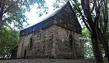 Photo en couleur d'un monument en pierre et au toit en bois au milieu d'arbres