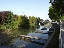 Photographie, prise depuis le quai, du canal de la Marne au Rhin et de ses pontons, avec en arrière-plan une péniche.