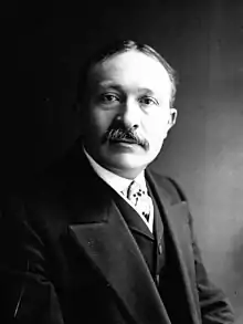 Photo en noir et blanc en buste en costume avec une moustache en chevron.