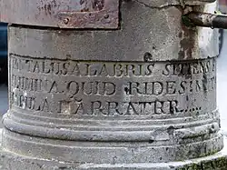 Détail de la base d'un pilier rond portant une inscription en latin apparaissant partiellement.