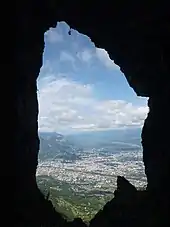 Agglomération cernée de montagnes vue « en médaillon&nbsp;» au travers des parois d'une grotte.