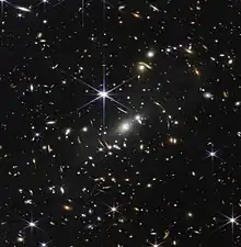 Photographie de format carré montrant une multitude de taches de diverses couleurs, formes et dimensions sur fond noir.