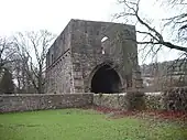 Photographie couleur d'une poterne à deux niveaux sous laquelle une arche ogivale permet de passer. Le niveau supérieur n'a plus de toit.