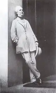 Photographie d'un homme debout adossé à un mur