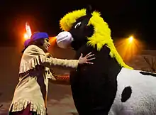 Homme déguisé en amérindien serrant un poney dans ses bras.