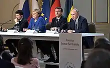 Quatre dirigeants installés à une table devant un parterre d'auditeurs, avec les drapeaux de leurs pays respectifs en arrière-plan.