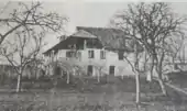 Photo noir et blanc d'une grande demeure située dans un verger avec des arbres sans feuilles.