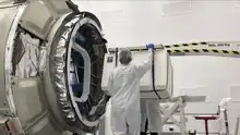 Deux personnes tenant le Cold Atom Laboratory devant un vaisseau Cygnus.